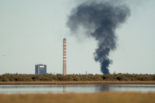 Fire and environmental pollution in an estuary with a factory and chimney in the background.