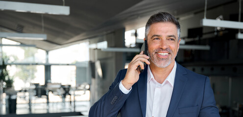 Happy wealthy successful mature business man talking on the phone in office. Smiling professional...