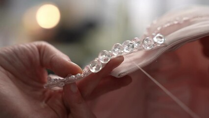 A woman's hand sews beads to a dress