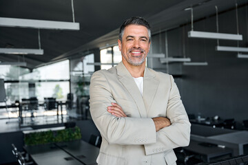 Fototapeta na wymiar Smiling confident middle aged business man, mature older professional successful company ceo corporate leader wearing beige suit standing in modern office arms crossed looking at camera, portrait.