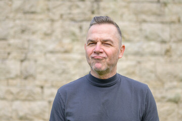 Grey haired man standing in front of a wall