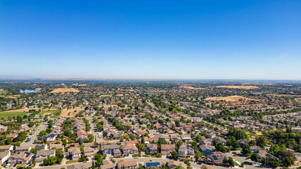 .A breathtaking aerial view of Antioch, California: houses nestled amidst verdant hills, crisscrossed by meandering streets, all under a picturesque blue sky.