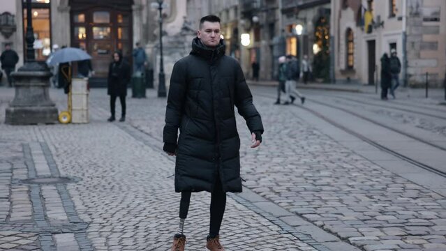 Disability walk, Medical prosthetic, Prosthetic leg. Young man, who has prosthetic leg due to his disability, is walking down street.