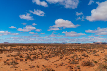 Wide arid African landscape with blue sky, clouds and yellow red dry soil.