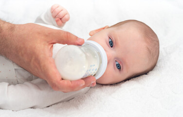 Baby eats formula from a bottle supported by his father