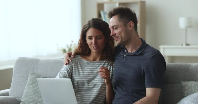 Pretty couple, e-services buyers sit on sofa choose goods, discuss travel tour, booking hotels, planning joint vacation, decide purchase via internet enjoy electronic shopping using modern technology