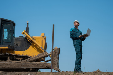 Caucasian male builder in hardhat holding laptop at construction site. 