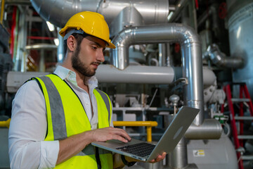Fototapeta na wymiar Professional male electrical engineer in safety uniform working on laptop at factory site control room. Industrial technician worker maintenance and checking power system at manufacturing plant room.