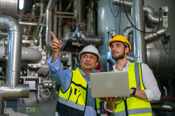 Two professional electrical engineer in safety uniform working together at factory site control room. Industrial engineer worker checking maintenance electric system on laptop computer at plant room.