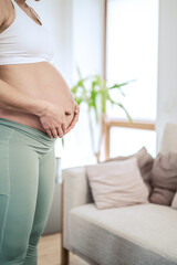 Lateral view of unrecognizable woman gently holding her belly in final months of pregnancy. Pregnancy first trimester - week 18. Side view. White flat background.
