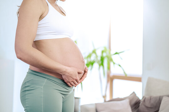 Lateral view of midsection of unrecognizable woman gently holding her belly in final months of pregnancy. Pregnancy first trimester - week 18. Side view. White flat background.