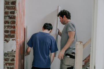 Two Caucasian male plasterer man checks the evenness of the walls after puttying.