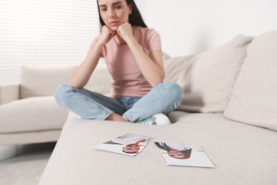 Upset woman looking at parts of torn photo in room, selective focus. Divorce concept