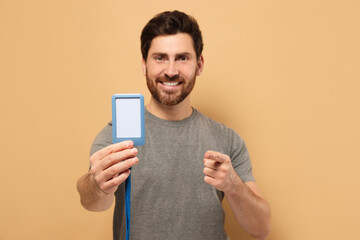 Happy man showing VIP pass badge against beige background, focus on hand