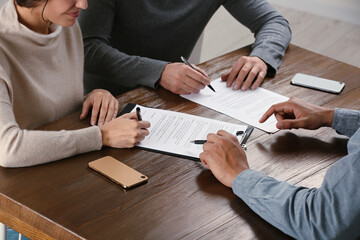 Notary helping couple with paperwork at wooden table, closeup