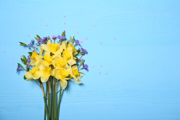 Bouquet of beautiful yellow daffodils and periwinkle flowers on light blue wooden table, top view. Space for text