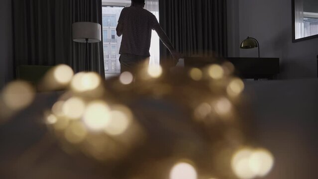A man sits in a luxury suite, approaching the window and talking on his mobile phone; light communication within a relaxed room.