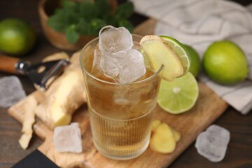Glass of tasty ginger ale with ice cubes and ingredients on wooden table, closeup