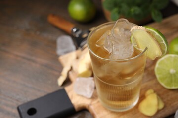 Glass of tasty ginger ale with ice cubes and ingredients on wooden table, closeup. Space for text