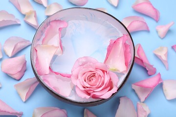 Bowl with water and rose petals on light blue background, above view. Spa composition