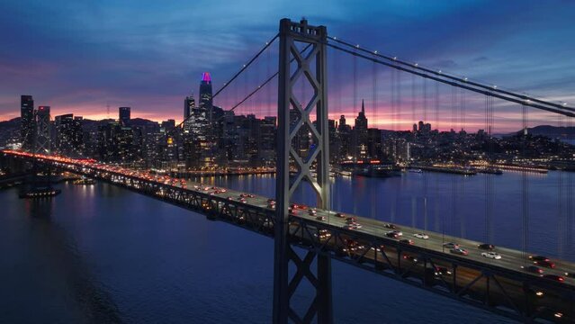 Still Aerial shot of Bay Bridge full of night traffic with downtown San Francisco on background. Financial district cityscape at dramatic colorful sunset sky. Cinematic San Francisco, California USA