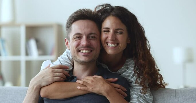 Close up young beautiful Latina wife hugs tightly with love and warmth to her Latin husband, smile look at camera pose at home. Newlyweds family, sincere feelings of spouses, happy harmonic marriage