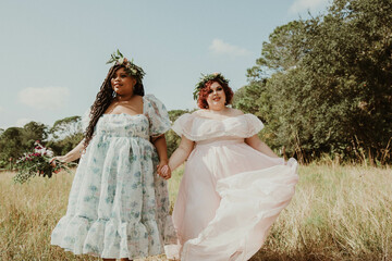 Fototapeta premium 2 plus size friends hold hands and walk in a field wearing dresses