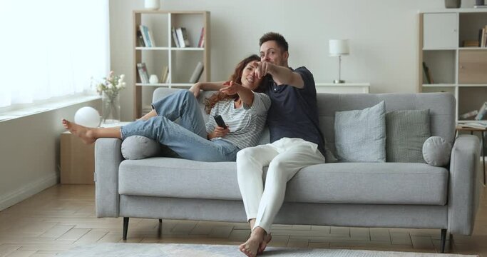 Millennial Hispanic young wife and husband talking, relaxing on sofa, discuss plot of TV series, blab while watching movie use on-line digital streaming services. Habit, communication, pastime at home