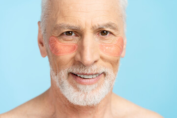 Portrait of handsome senior pensioner with patches under eyes isolated on blue background