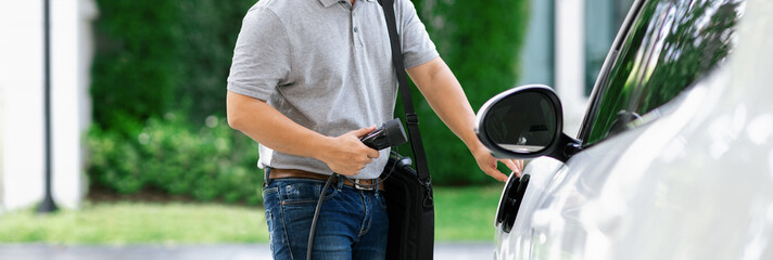 Progressive asian man install cable plug to his electric car with home charging station in the...