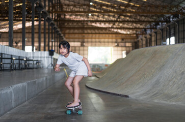 Obraz na płótnie Canvas asian child skater or kid girl playing skateboard or ride carving surf skate barefoot to wave ramp or wave bank and fun in indoor skate park by extreme sports surfing surfskate to wears white t-shirt