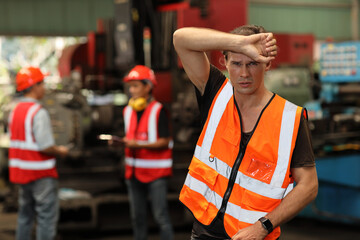 Tired technician engineer in protective uniform standing and taking a break while wipe the sweat...