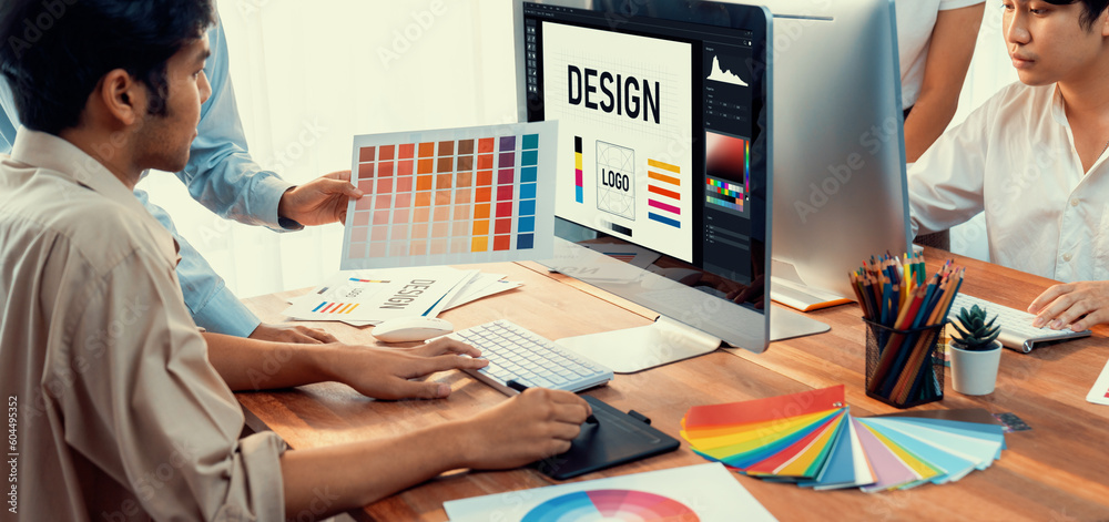 Poster Graphic designer work on computer laptop and with graphic drawing pen while brainstorming unique design with professional graphic team in modern digital studio workplace. Panorama shot. Scrutinize