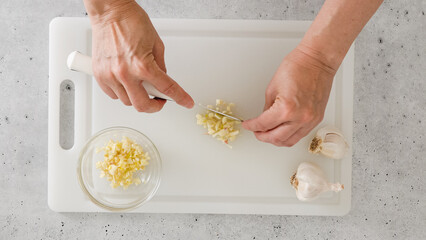 The chef chopping garlic on a white plastic cutting board, close-up view, preparation process
