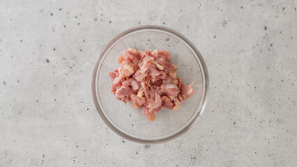 Chopped raw chicken fillet close-up in a glass bowl on a gray stone background, flat lay