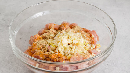 Chopped chicken fillet marinated with soy sauce, seasoning, turmeric, and fresh chopped garlic close-up in a glass bowl