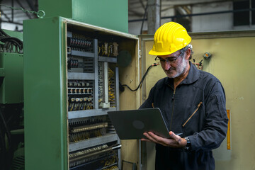 Electrical Engineer team working front control panel, An electrical engineer is installing and using a tablet to monitor the operation of an electrical control panel in a factory service room.