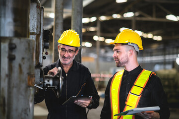 Two operators inspecting machines in industrial factory, holding documents and tablet for check, background in industrial warehouse., middle-aged male worker, Caucasian.