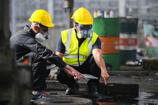 Two officers wearing gas masks inspected the area of a chemical leak in an industrial warehouse to assess the damage. Technicians wearing gas masks inspect and assess the recovery of toxic spills.