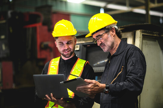 Two industrial operators standing holding laptops and tablets, industrial warehouse warehouse background, middle-aged male worker, Caucasian.