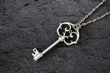 Old silver simple key on a chain on stone dark background, macro.