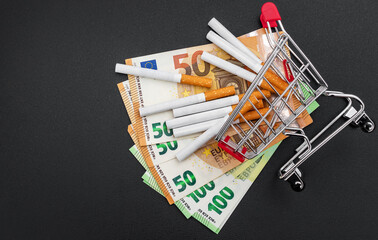 Shopping cart with cigarettes and euro bills on black.