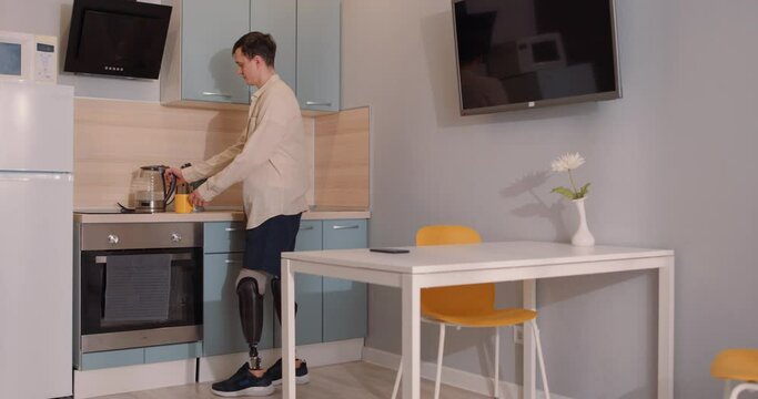 handsome disabled man standing in artificial fake legs drinking coffee or tea in kitchen, spending morning routine. disabled caucasian man with prosthesis enjoy morning or day. happy disabled person