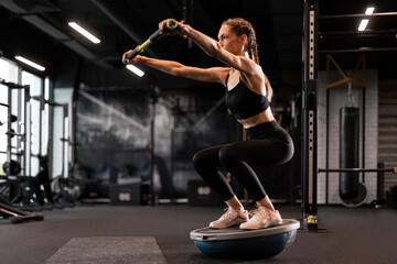 Sporty woman making squats on balance trainer.