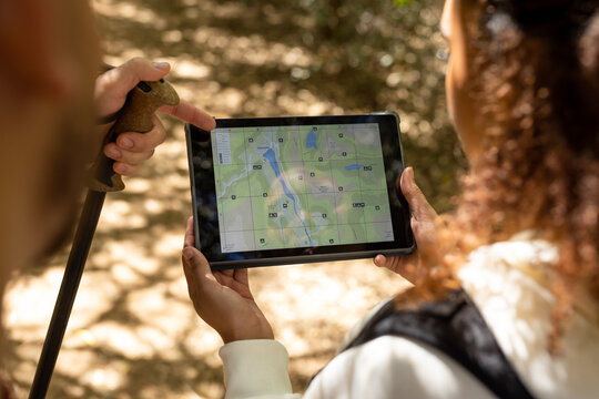 Biracial couple using tablet with map in forest