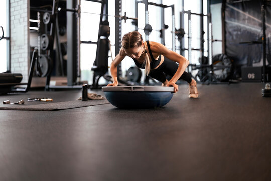 Portrait of a muscular woman on a plank position with bosu at gym.