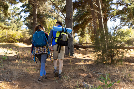 Biracial couple wearing backpacks and hiking in forest