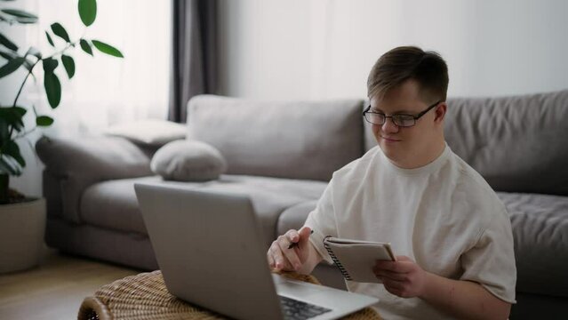 Down syndrome young adult man sitting at home, using laptop for learning