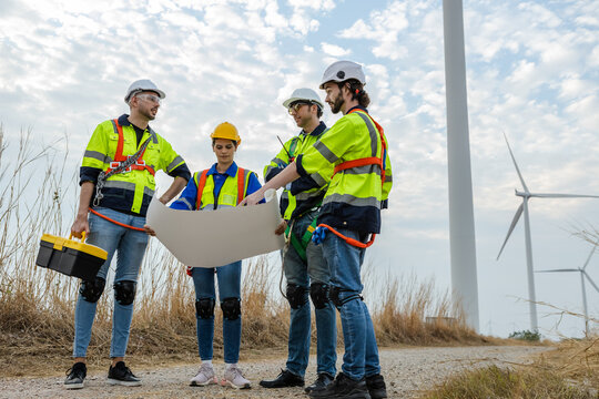 Teamwork engineer worker wearing safety uniform holding and reading blueprint at wind turbine field renewable energy. technology protect environment reduce global warming problems.