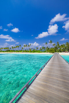 Luxury travel landscape. Water villas, wooden pier bridge leads to palm trees over white sandy shore close to blue sea, seascape. Summer panoramic vacation, beach resort on tropical island paradise